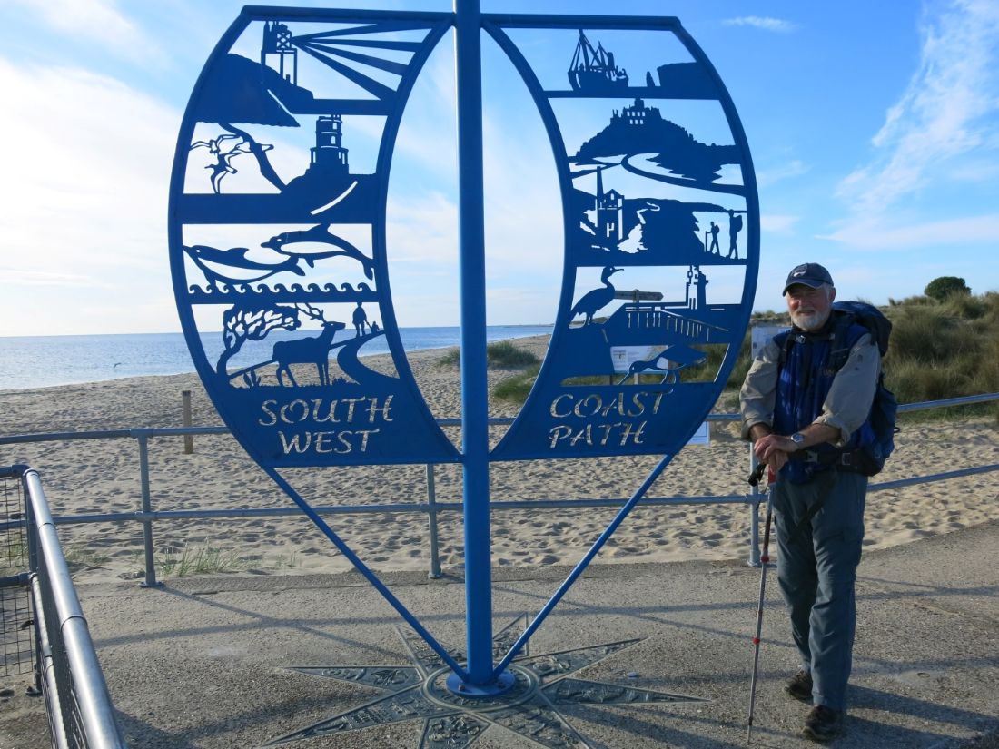South West Coast Path walker pauses beside the trail sign near a beach |  Peter Wells
