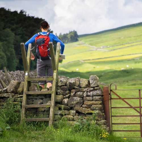A hiker crossing a stile on the Hadrian's Wall Walk in Northumberland, Northeast of England, UK.