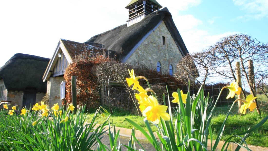 Flowers blossom outside the thatched church of Freshwater Bay - Walkers' Britain