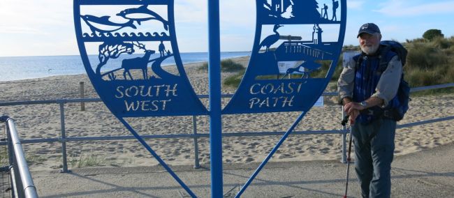South West Coast Path walker pauses beside the trail sign near a beach | Peter Wells